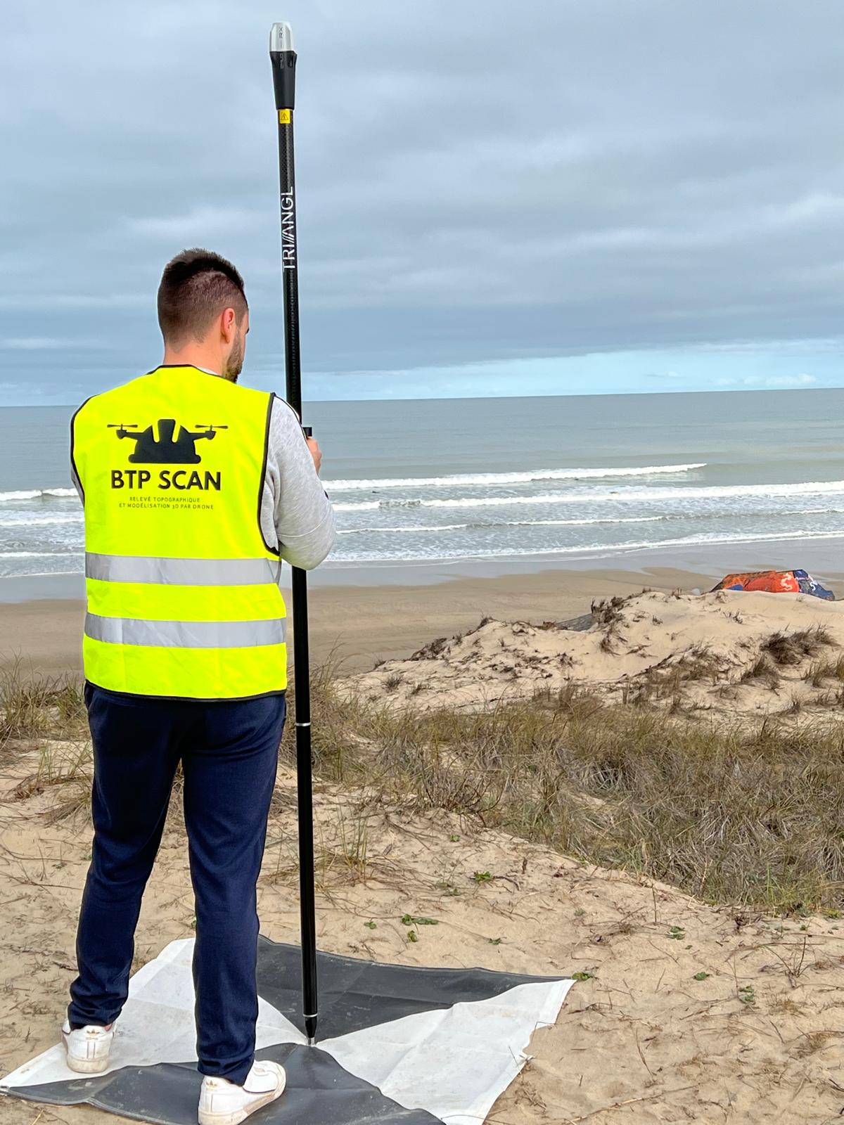 Homme en gilet jaune avec équipement de topographie sur la plage